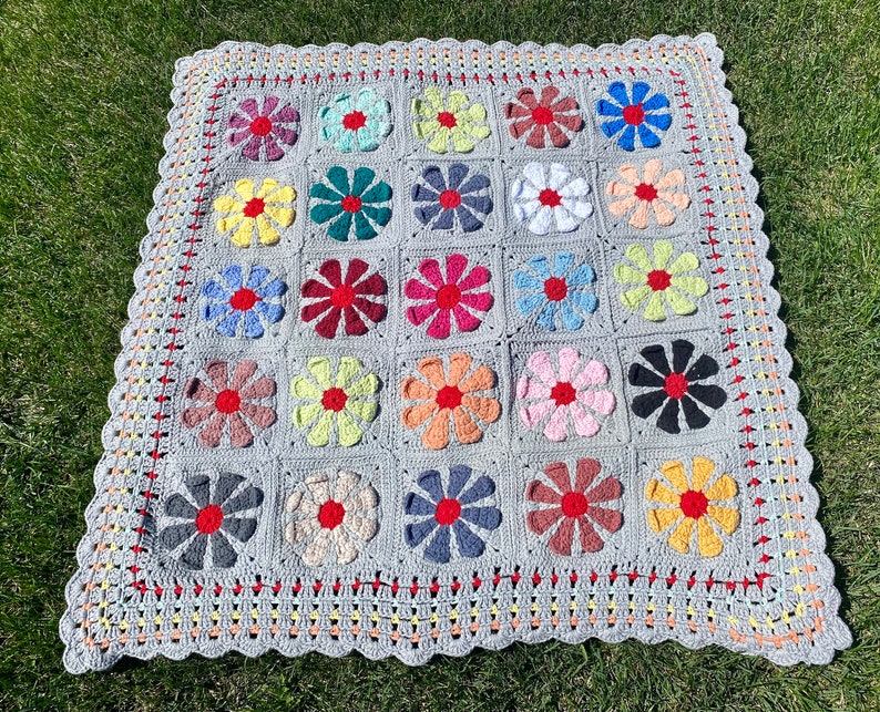 Puede incluir: Una manta de ganchillo gris con un borde festoneado. La manta est&aacute; hecha de cuadrados con dise&ntilde;os de flores de colores en tonos de rojo, amarillo, azul, verde y rosa.