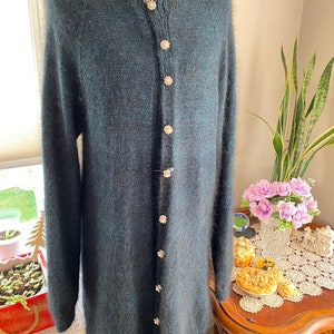 May include: A long, dark green cardigan with a fuzzy texture and a row of decorative buttons down the front.