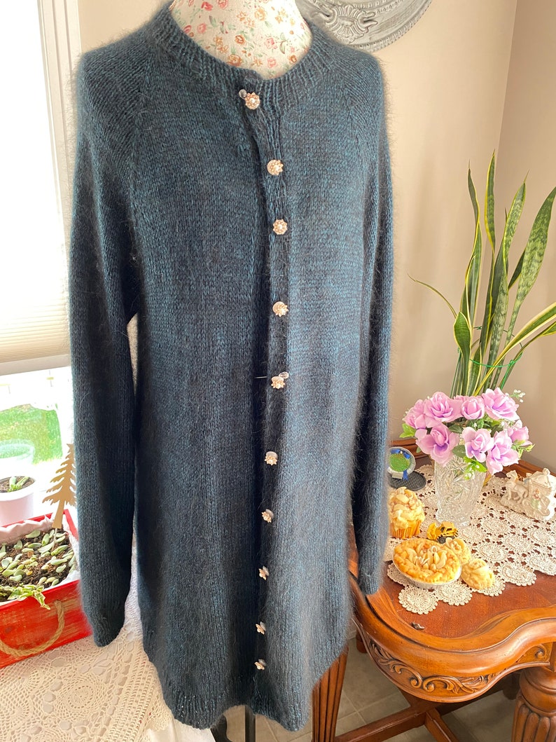 May include: A long, dark green cardigan with a fuzzy texture and a row of decorative buttons down the front.