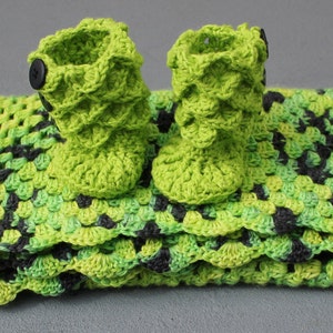 May include: A green crocheted baby blanket with a scalloped edge and two matching green crocheted booties with black buttons.