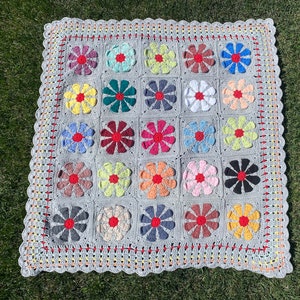 Puede incluir: Una manta de ganchillo con fondo gris y dise&ntilde;os de flores de colores. La manta est&aacute; hecha con una variedad de colores, incluyendo rosa, azul, verde, amarillo y rojo.