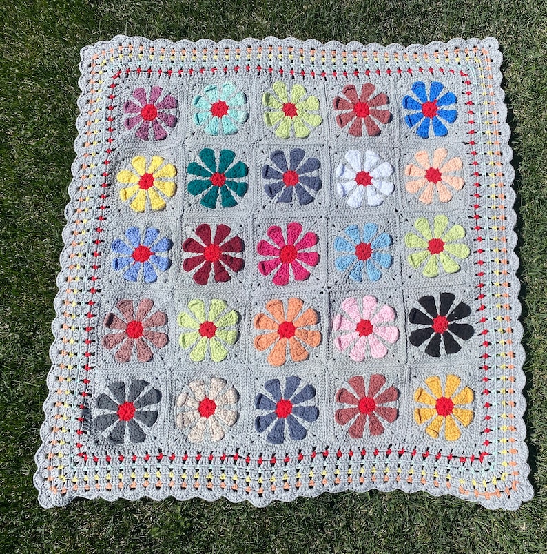 Puede incluir: Una manta de ganchillo con fondo gris y dise&ntilde;os de flores de colores. La manta est&aacute; hecha con una variedad de colores, incluyendo rosa, azul, verde, amarillo y rojo.