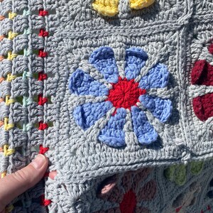 Puede incluir: Una manta de ganchillo con fondo gris y dise&ntilde;os de flores de colores. La manta est&aacute; hecha con hilo de diferentes colores y tiene una superficie texturizada.