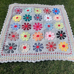 Puede incluir: Una manta de ganchillo con fondo gris y dise&ntilde;os de flores de colores. La manta tiene un borde festoneado y est&aacute; hecha con una variedad de hilos de colores diferentes.