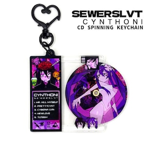 May include: A keychain featuring a black heart-shaped clasp and a rectangular tag with the text "CYNTHONI" and a list of song titles. A clear plastic disc with a purple anime character design is attached. The text "SEWERSLVT CYNTHONI CD SPINNING KEYCHAIN" is at the top.
