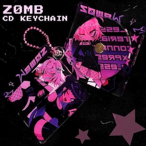 May include: A ZOMB CD keychain with a pink chain. The keychain features anime-style illustrations in pink, black, and purple. The text "ZOMB CD KEYCHAIN" is displayed in white block letters. The CD case is open, revealing a CD with text.