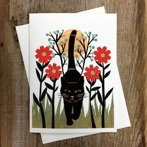 May include: A black cat walks through a field of red flowers with green foliage. The cat is silhouetted against a yellow sun.
