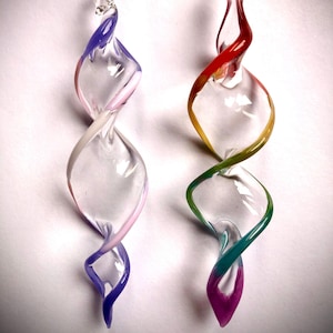 May include: Two glass ornaments with a spiral design. The ornament on the left is clear with pink, white, and purple stripes. The ornament on the right is clear with red, yellow, green, and purple stripes.