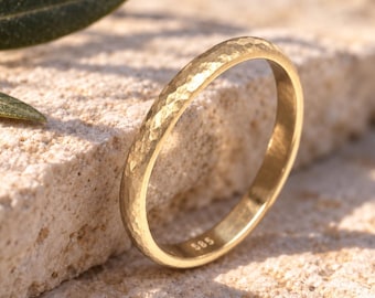May include: A gold ring with a hammered, textured surface and a rounded profile. The interior of the band is clearly stamped with the number 585, indicating the gold purity. The ring has a polished finish that reflects light across its surface.