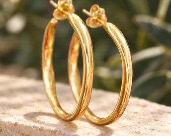 May include: A pair of gold hoop earrings with a smooth, polished finish. Each earring features a circular design with a post back closure, showcasing a reflective metallic surface that catches the light, creating a bright and warm appearance.