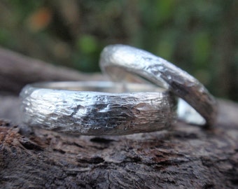 May include: Two silver wedding bands with a textured, hammered finish. The bands are stacked on top of each other.