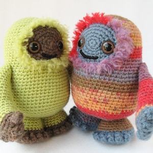 May include: Two crocheted stuffed animals. One is green with a brown face and brown feet. The other is multi-colored with a blue face and blue feet.