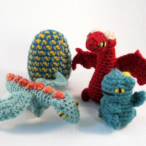 May include: Four crocheted dragon toys, two blue, one red, and one blue and yellow egg-shaped. The blue dragons have orange accents and the red dragon has white accents.