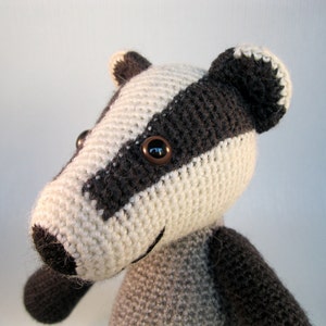 May include: Close-up of a crocheted badger stuffed animal with black eyes and a white and gray striped pattern.