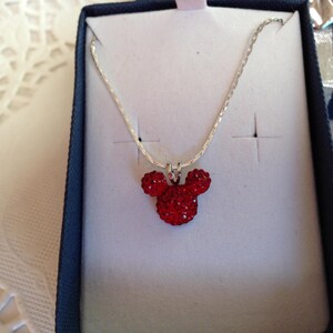 May include: A silver chain necklace with a red crystal Mickey Mouse head pendant.