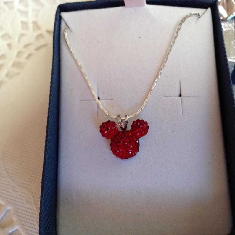 May include: A silver chain necklace with a red crystal Mickey Mouse head pendant.