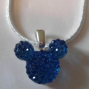 May include: A blue crystal pendant in the shape of a mouse head with a silver chain. The pendant has a silver bail and is made of many small, sparkling blue crystals. The chain is a silver snake chain.