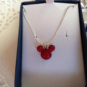 May include: A silver chain necklace with a red rhinestone Mickey Mouse pendant.