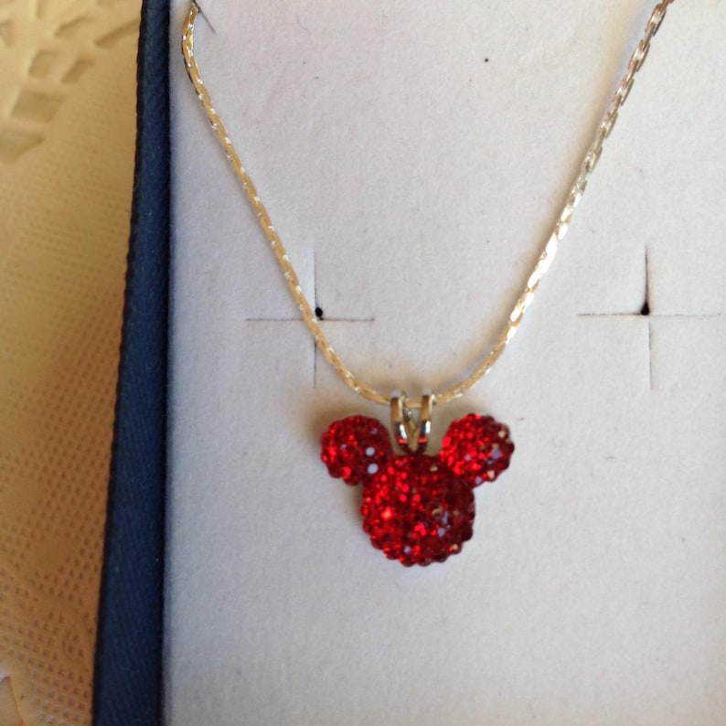 May include: A silver chain necklace with a red rhinestone Mickey Mouse head pendant.
