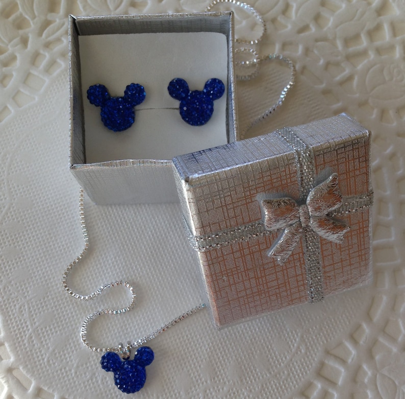 May include: A silver gift box with a bow, a pair of blue rhinestone Mickey Mouse earrings in an open box, and a matching necklace with a pendant. The jewelry is displayed on a white surface.