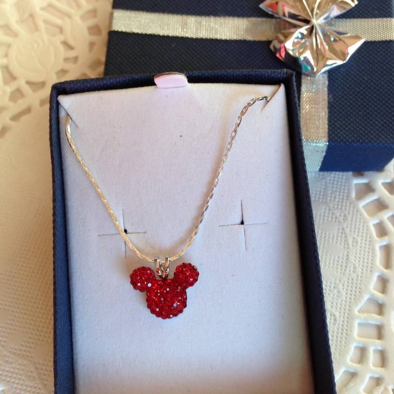 May include: A silver chain necklace with a red rhinestone Mickey Mouse pendant in a blue gift box.