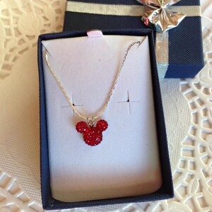 May include: A silver chain necklace with a red crystal Mickey Mouse pendant in a blue gift box.