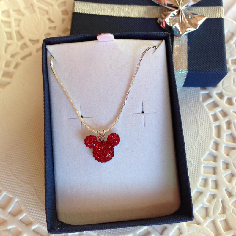 May include: A silver chain necklace with a red crystal Mickey Mouse pendant in a blue gift box.
