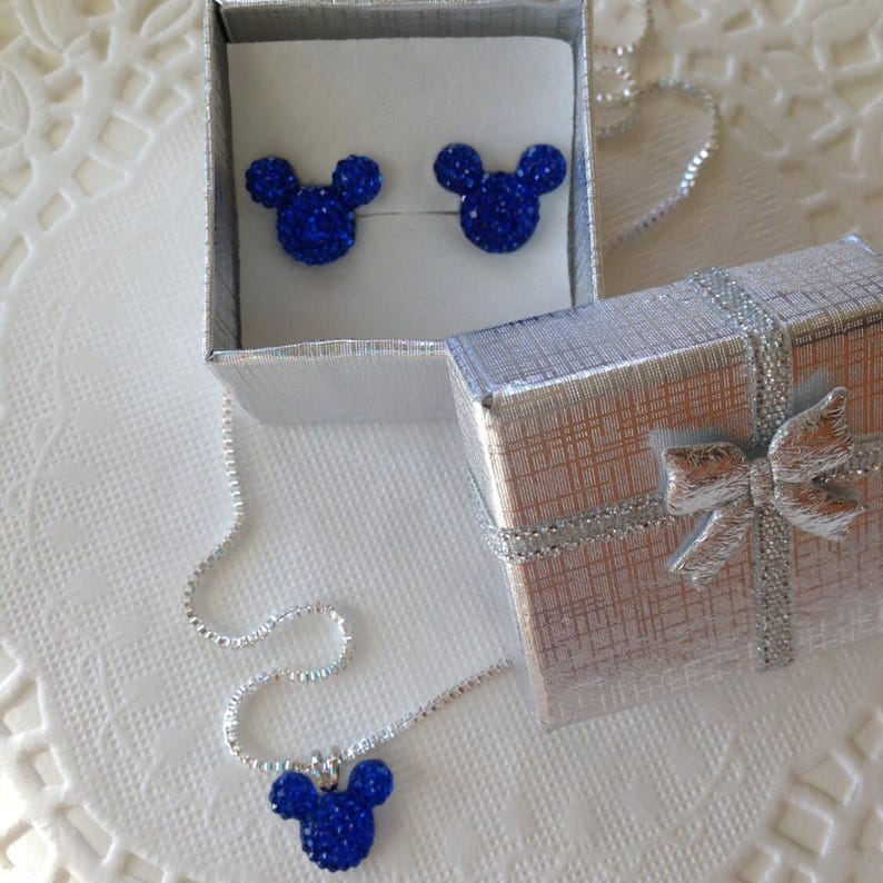 May include: A jewelry set featuring a necklace and earrings in a gift box. The necklace has a silver chain with a blue Mickey Mouse pendant. The earrings are also blue Mickey Mouse shapes. The gift box is silver with a bow.