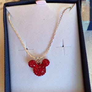 May include: A silver chain necklace with a red crystal Mickey Mouse head pendant.