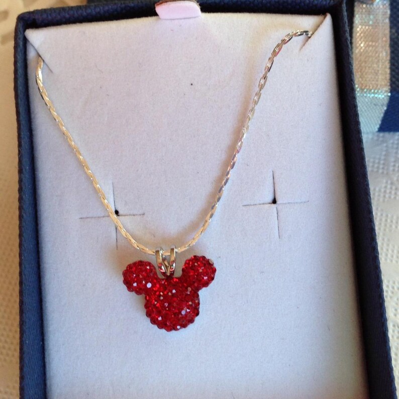 May include: A silver chain necklace with a red crystal Mickey Mouse head pendant.