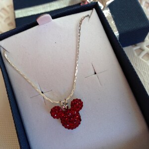 May include: A silver chain necklace with a red rhinestone Mickey Mouse head pendant.