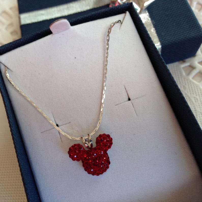 May include: A silver chain necklace with a red rhinestone Mickey Mouse head pendant.