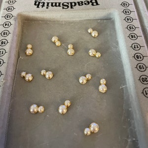 K&ouml;nnte beinhalten: Eine Ansammlung von perlenartigen Schmucksteinen mit goldfarbenen Fassungen. Die Schmucksteine sind auf einem grauen Beadboard angeordnet, mit dem Markennamen "BeadSmith". Die Schmucksteine sind in Gruppen von zwei und drei.