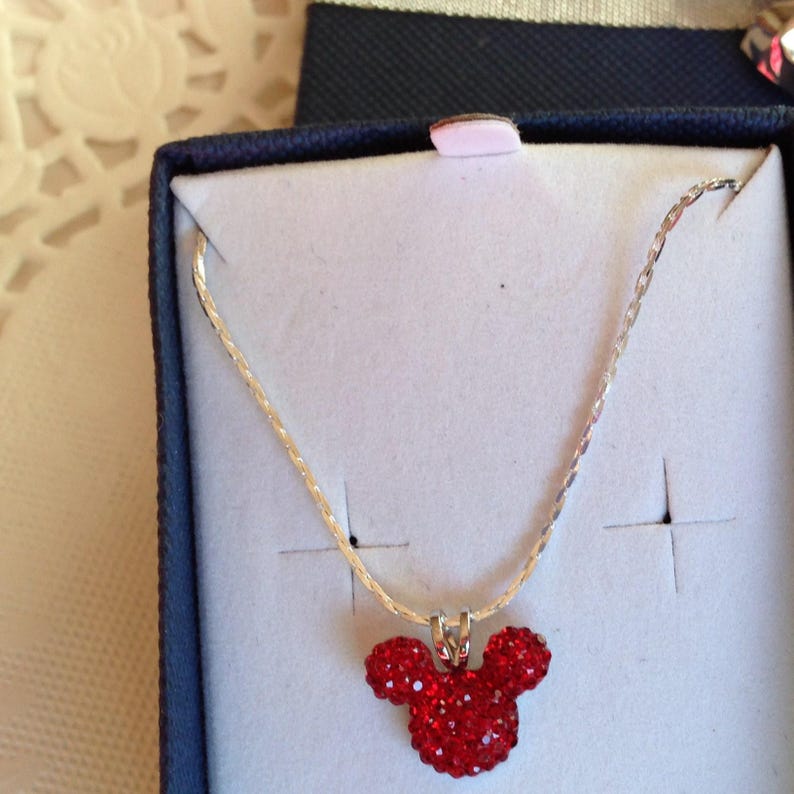 May include: A silver chain necklace with a red rhinestone Mickey Mouse head pendant.