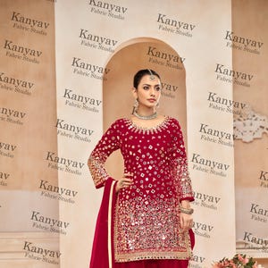 May include: A woman is wearing a red salwar kameez with mirror work embroidery. The outfit is paired with a matching dupatta. The fabric is a soft, flowing material. The outfit is perfect for special occasions.