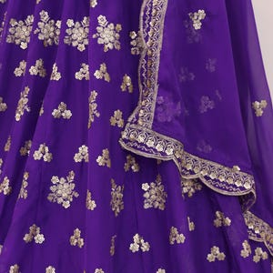 May include: A vibrant purple garment with intricate gold floral embroidery. The fabric appears to be a flowing material, possibly silk or chiffon. The design includes a decorative border with gold embellishments.