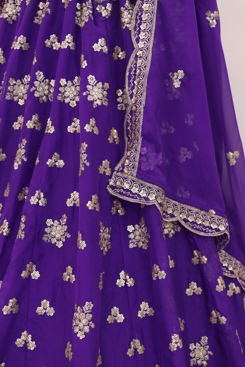 May include: A vibrant purple garment with intricate gold floral embroidery. The fabric appears to be a flowing material, possibly silk or chiffon. The design includes a decorative border with gold embellishments.