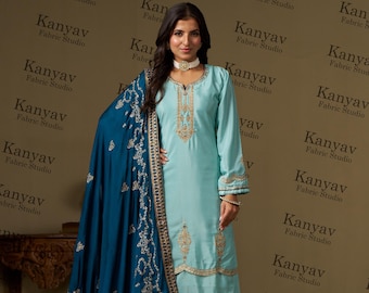 May include: A light blue salwar kameez with gold embroidery and a teal dupatta. The outfit is worn by a person with a necklace and earrings.