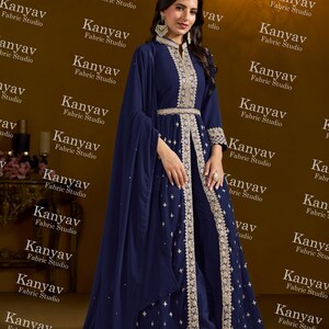 Pode incluir: Um traje formal azul marinho com bordados dourados, incluindo uma jaqueta de manga comprida e cal&ccedil;as a condizer. O traje inclui uma longa capa fluida e &eacute; da Kanyav Fabric Studio.