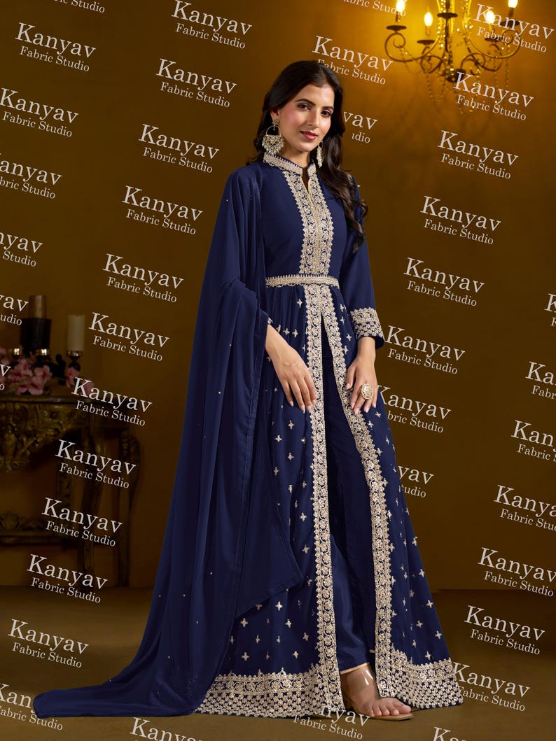 Pode incluir: Um traje formal azul marinho com bordados dourados, incluindo uma jaqueta de manga comprida e cal&ccedil;as a condizer. O traje inclui uma longa capa fluida e &eacute; da Kanyav Fabric Studio.