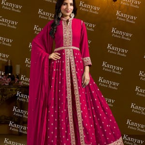 Pode incluir: Um vestido formal magenta com bordados dourados. O vestido apresenta gola alta, mangas compridas e uma saia fluida. O vestido &eacute; adornado com bordados dourados ao longo do decote, mangas e bainha. O vestido &eacute; da Kanyav Fabric Studio.
