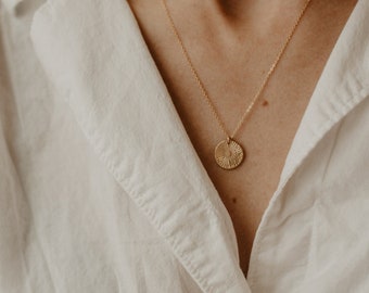May include: A close-up of a person wearing a white button-down shirt with a gold necklace featuring a textured circular pendant.