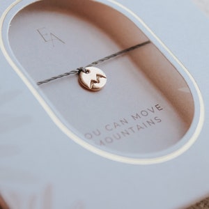 May include: A gray box with a gold-filled mountain charm bracelet inside. The box has the text "1/4 Karat Gold-Filled" and "Ever Aster" on it. The bracelet has the text "You Can Move Mountains" on the box.