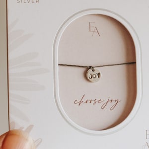 May include: A sterling silver bracelet on a white display card. The bracelet features a small round charm stamped with the word JOY. The card displays the text EA, EVER ASTER, and the phrase choose joy in a script font.