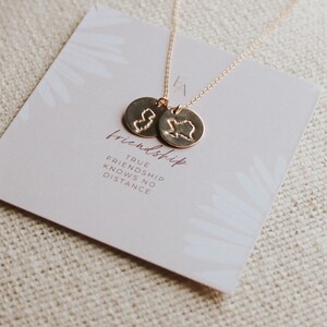 May include: A gold necklace with two circular pendants, each with a state outline. The necklace is displayed on a card with the word "friendship" and the phrase "True friendship knows no distance."