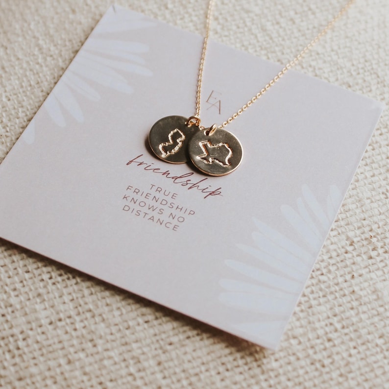 May include: A gold necklace with two circular pendants, each with a state outline. The necklace is displayed on a card with the word "friendship" and the phrase "True friendship knows no distance."
