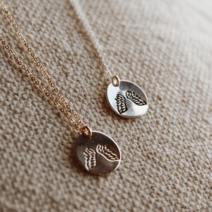 Puede incluir: Dos collares de plata con colgantes de alas de &aacute;ngel. Los collares est&aacute;n sobre un fondo de tela beige.