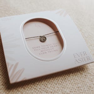 May include: A sterling silver charm bracelet with a small, round pendant. The bracelet is displayed on a light pink card with the text "SOME THINGS JUST FILL YOUR HEART WITHOUT EVEN TRYING" and the brand name "EVER ASTER".