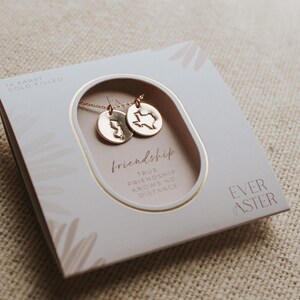 May include: A gold-filled necklace set with two pendant necklaces, each with a circular charm. One charm depicts the outline of New Jersey, the other Texas. The box reads "friendship, true friendship knows no distance."