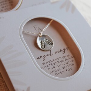 Puede incluir: Una caja blanca con un collar de plata con un peque&ntilde;o colgante redondo con alas de &aacute;ngel. La caja tiene el texto "sterling silver" y "angel wings". El texto en la caja dice: "Dondequiera que vayas, lo que sea que hagas, que tu &aacute;ngel de la guarda te cuide." La caja tambi&eacute;n tiene el texto "Ever After".
